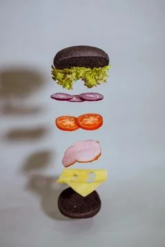 Flying hamburger divided into components - tomato, onion, cheese, cabbage, .. Stock Photos