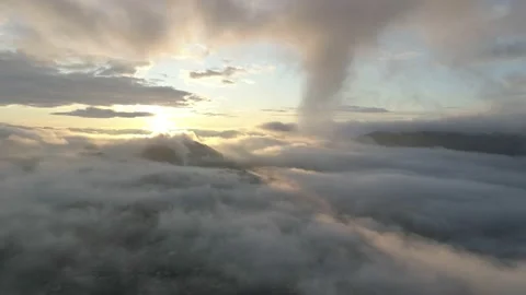 Flying high over the clouds, revealing misty landscape with bright morning sun Stock Footage 147930839
