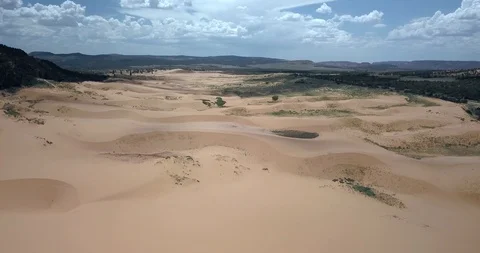 Flying high over rolling clean sand dunes and grass next to mountains Stock Footage 119121748