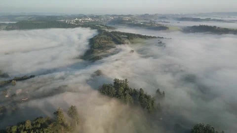 Flying high over woods and green fields shrouded in mist. Low clouds. Stock Footage 253362653