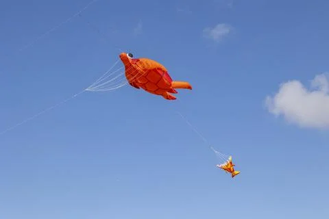 Flying inflatable orange turtle kite with stabilizing fish tail and blue lift Stock Photos