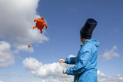 Flying inflatable orange turtle kite with stabilizing fish tail and blue lift Stock Photos