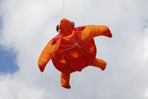 Flying inflatable orange turtle kite with stabilizing fish tail and blue lift Stock Photos