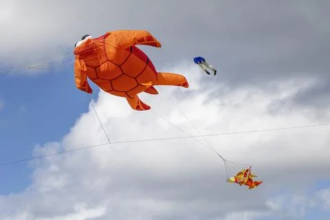 Flying inflatable orange turtle kite with stabilizing fish tail and blue lift Stock Photos