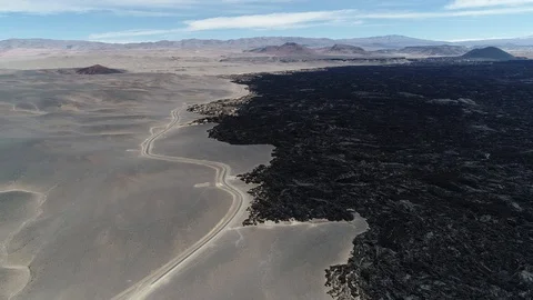 Flying at the limit of black bed of lava and desert with road. Volcanic textures 動画素材 103482095