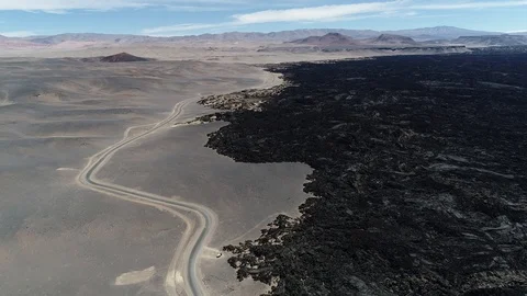 Flying at the limit of black bed of lava and desert with road. Volcanic textures Stockbeeldmateriaal 103482134