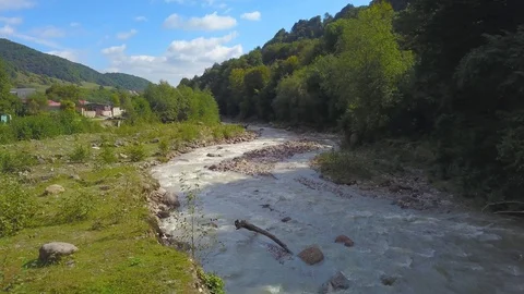 Flying low above mountain river among green trees and mountain village Stock Footage 99229112