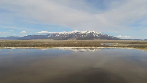 Flying low and slow over a still pond reflecting snow-covered Mt Blanca Stock Footage 107613683