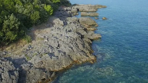Flying low over Adriatic coast line with stones green bushes and clear sea water Stock Footage 78007140