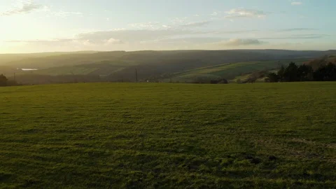 Flying low over grassy meadow with fields, farmland and lake during sunset Stock Footage 122149995