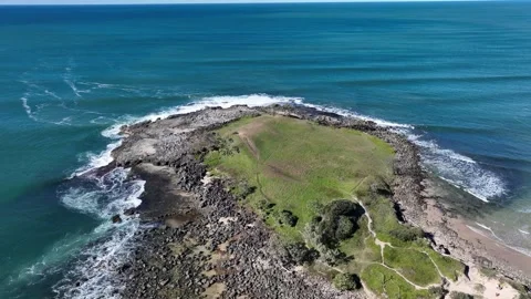 Flying low over rocky grass topped headland, below are faoming waves crashing Stock Footage 331017941
