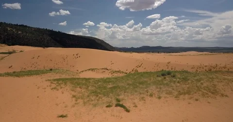 Flying low over rolling sand dunes and grass next to mountains Stock Footage 119121601