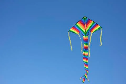Flying multicoloured kite against clear blue sky Stock Photos