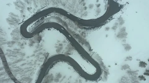 Flying over bend in road on a mountain pass, a winter cloudy day with snowfall a 스톡 동영상 236401147