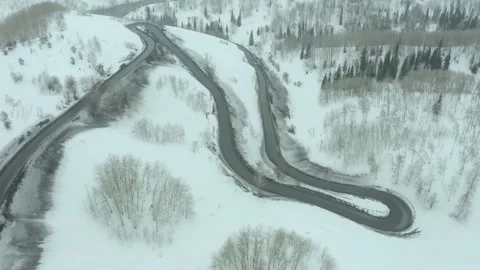 Flying over bend in road on a mountain pass, a winter cloudy day with snowfall a Stock Footage 236401944