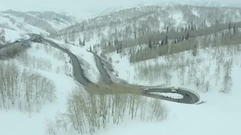 Flying over bend in road on a mountain pass, a winter cloudy day with snowfall a Stock Footage 236403130
