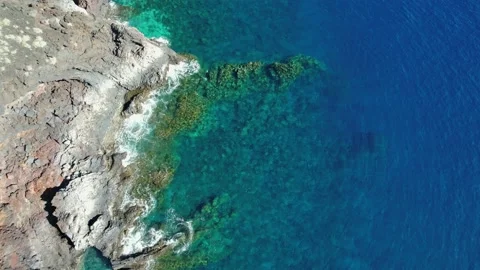Flying over a blue ocean with clear underwater seascape near a volcanic coast Stock Footage 230294591