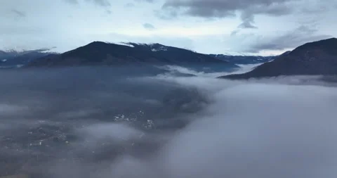 Flying over the clouds and fog revealing a small village and the snowy mountains Stock Footage 174436859