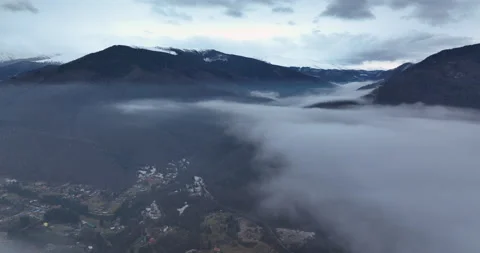 Flying over the clouds on top of a small village with a mountain backdrop. Stock Footage 174423729