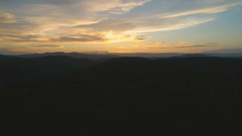 Flying up over dark mountain forest. View of clouds and golden hour sunset Video stock 108108152