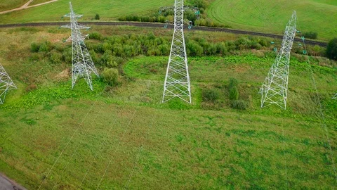 Flying over electrical pylons with wires lines on green field near railway. Stockbeeldmateriaal 122687795