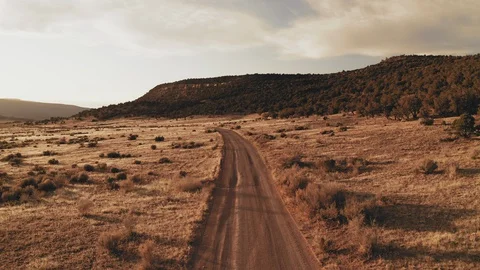 Flying over an empty dirt road through sagebrush prairie at sunset Stock Footage 128660146