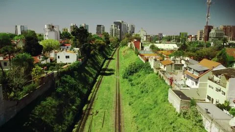 Flying over empty railroad track, rail way in green grass among city buildings Stock Photos