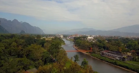 Flying over forest under mountain and orange bridge with panorama of Vang Vieng Stock Footage 108469291