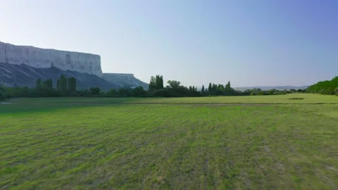 Flying over a green field surrounded by trees outside the city at dawn and Stock Footage 152315197