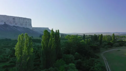 Flying over a green field, trees and road at dawn and against the backdrop of Stock Footage 152315521