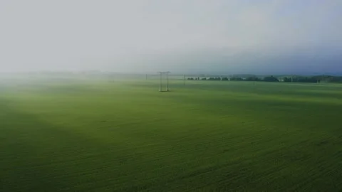Flying over green fields along high voltage towers of power lines at dawn. Stockbeeldmateriaal 156198251