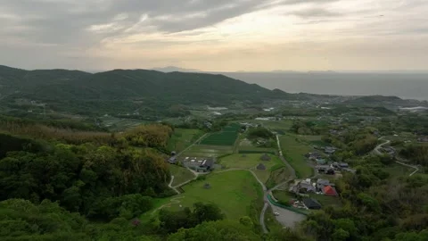 Flying over green hilltop to fields and farms in small coastal village Stock Footage 240890590