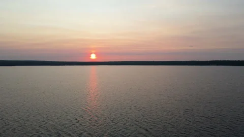 Flying over lake on a cloudy day with views of orange sunset over tree covered Vídeo Stock 313665250