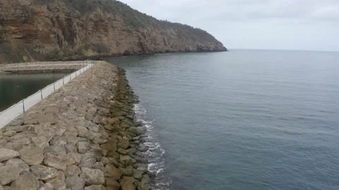 Flying over a large stone pier protecting a village from the waves Stock Footage 146755698
