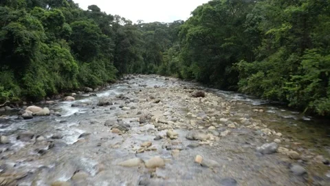 Flying over a large tropical river full of boulders and rocks while raining Stock Footage 151279377