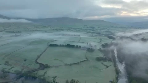 Flying over meandering river towards mist shrouded patchwork fields at Video stock 276053006