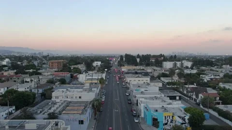 Flying over Melrose Avenue in Los Angeles at sunset with Downtown LA in Stock Footage 213988404