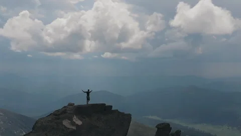 Flying over the mountain top on which stands a man raising his hands. Drone shot Video stock 92552298