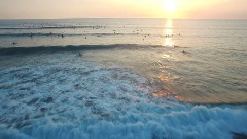 Flying over ocean with lots of surfers waiting in the water to the sunset Stock Footage 81214493