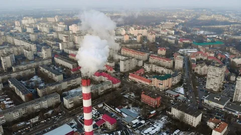 Flying over a red-white pipe with thick smoke going over the city.  Video stock 102703223