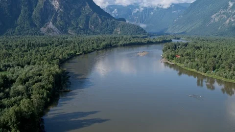 Flying over a river that flows into a lake against the backdrop of mountains 4k Stock Footage 125124963