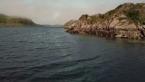 Flying over a river next to a rocky shore with mountains in the background Stock Footage 224138845