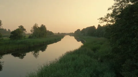 Flying over River Surrounded by Large Green Forest at Sunset Time Stock Footage 68399849