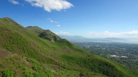 Flying Over Rolling Green Mountains with City in the Background Vídeos de archivo 77109595