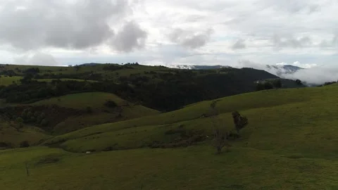 Flying over rolling hills and fields towards low clouds in a valley Stock Footage 130957983