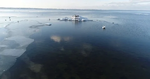 Flying over sandy beach with rolling waves and drifting ice floes in winter sea. Video stock 86700275