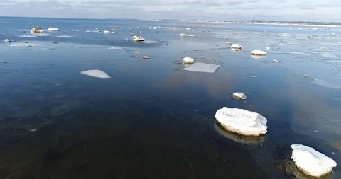 Flying over sandy beach with rolling waves and drifting ice floes in winter sea. Stock Footage 86702293
