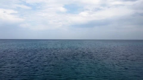 Flying over sea water with cloudy sky and horizon line in the background Stock Footage 245543997