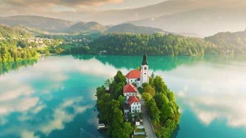 Flying over small island on Bled Lake in Slovenia, warm morning sun, light fog Stock Footage 232776908
