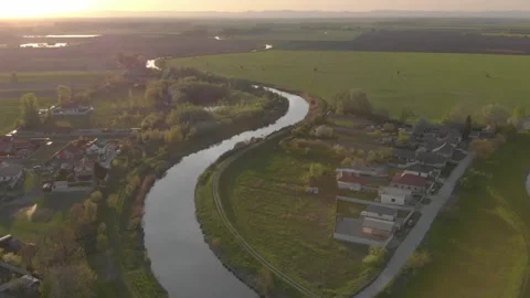 Flying over a small river and rural vilage in the sunset Stock Footage 232487289